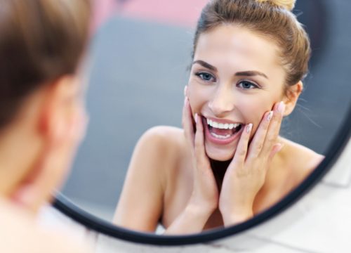 Woman looking at her face in the mirror after using Colorescience® Skincare