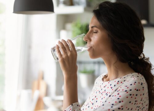 Photo of a woman drinking a glass of water at home in her kitchen