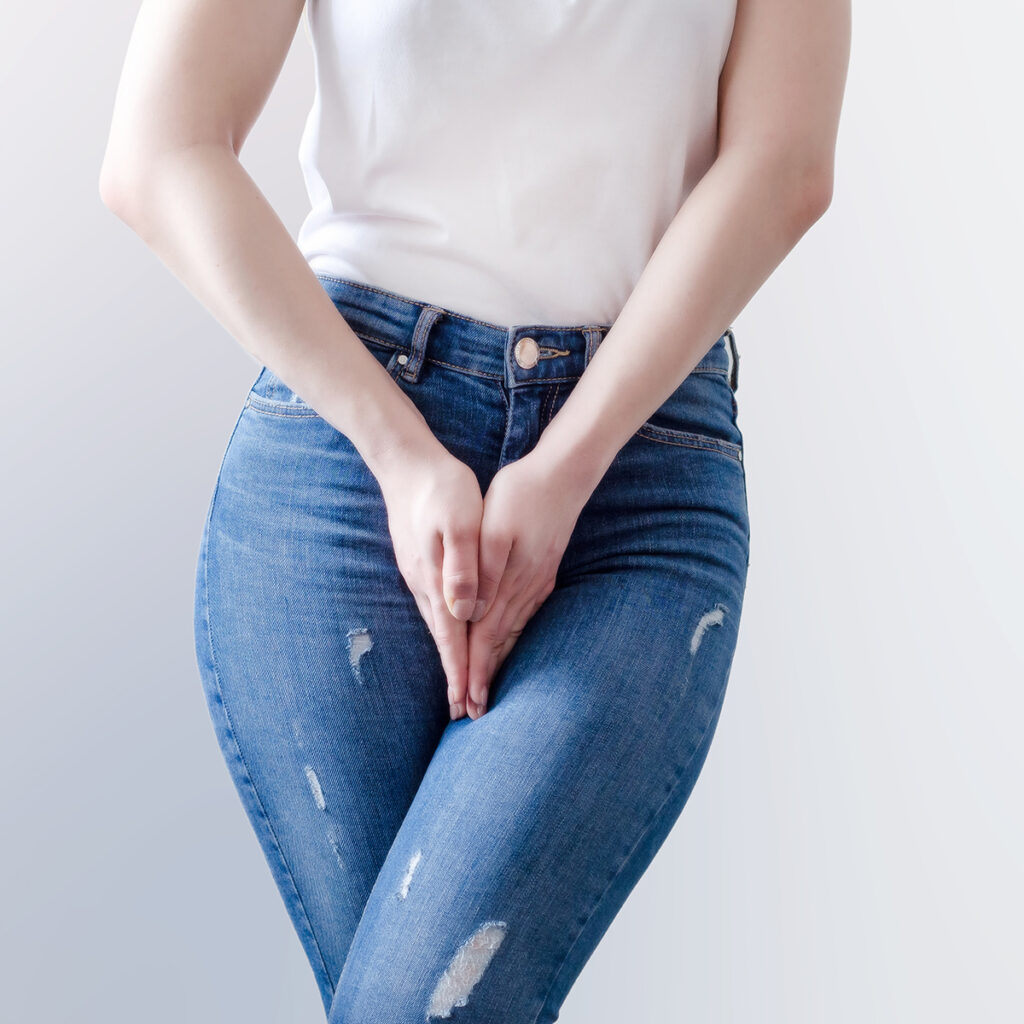 Photo of a woman in jeans placing her hands in front of her pelvis