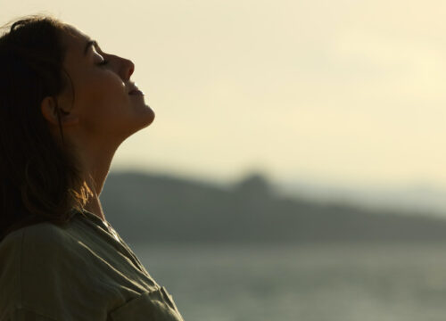 Photo of a woman standing by a lake feeling relief and peace